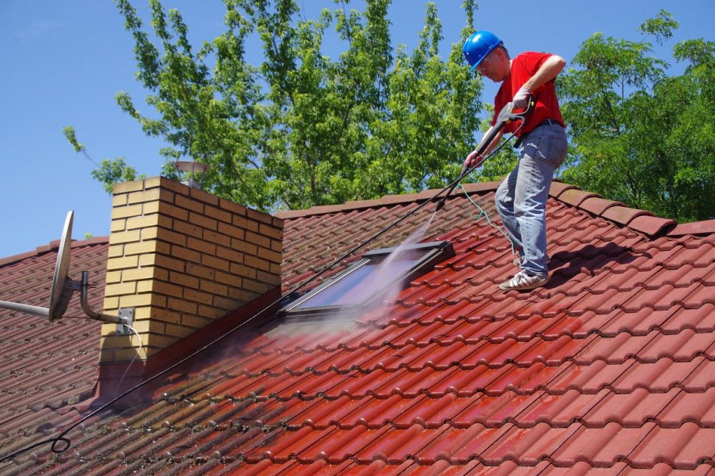 Artisan couvreur utilisant un nettoyeur haute pression sur une toiture en tuiles